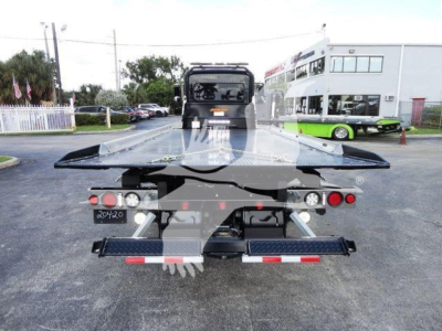 Peterbilt 337 rollback truck rear view showing flatbed and equipment, stock number J03058, dealership lot in background.