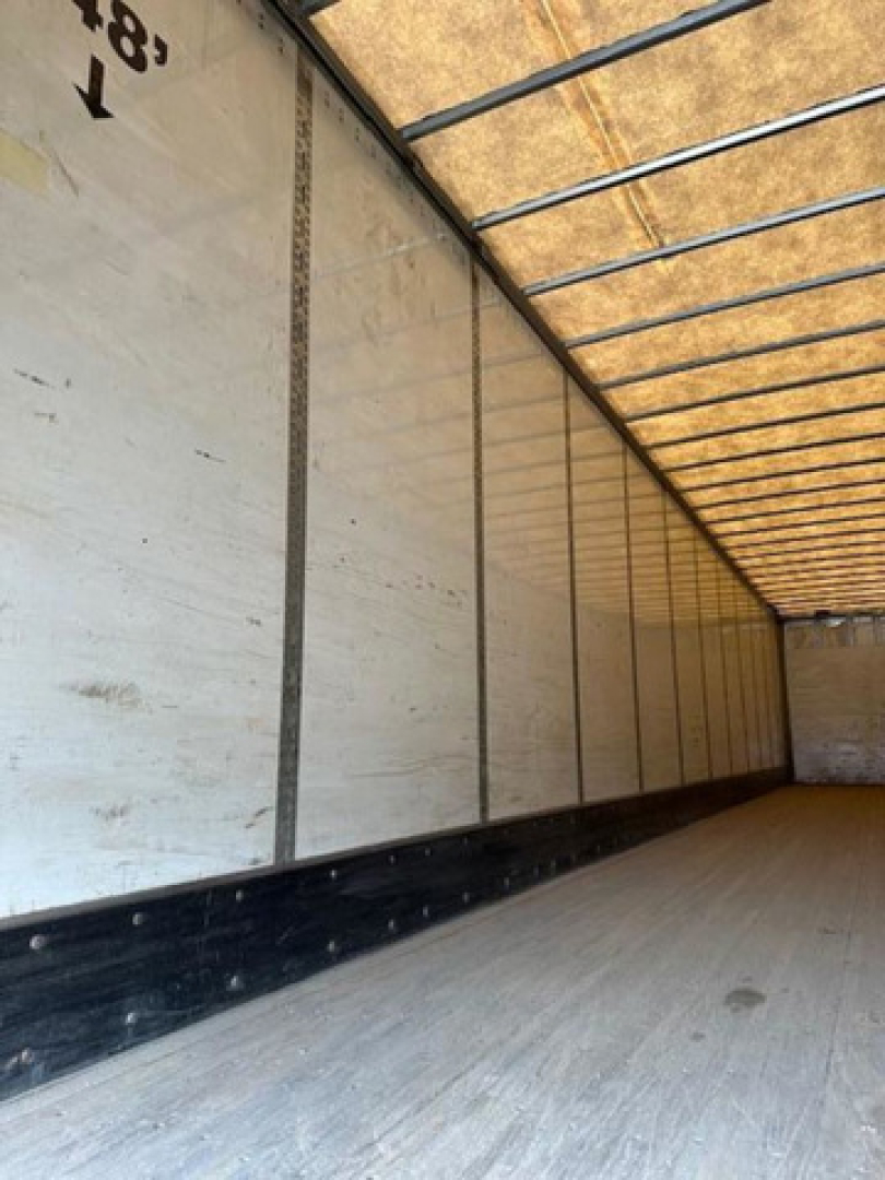 Truck trailer interior showing empty cargo area with white sidewalls and wooden ceiling beams.