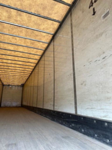 Trailer interior showing empty cargo area with side walls, roof ribs, and wooden floor. Texts: 46? and arrows on right wall. VIN and stock not legible here.