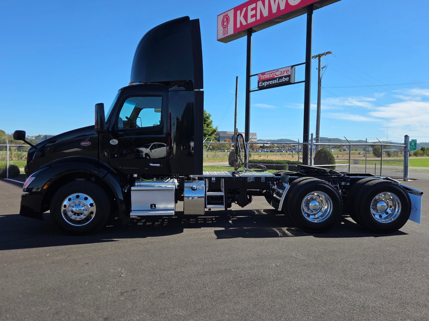 Peterbilt 579 conventional daycab truck in profile view with hood open; chrome wheels; fuel tanks; no cargo; no trailer attached. Visible text includes Kenworth sign in background.