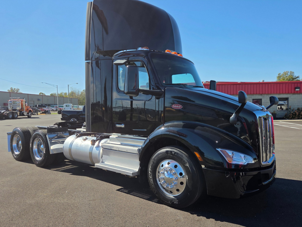 Peterbilt 579 conventional daycab tractor in black, side view, with tall sleeper and chrome fuel tanks, triple rear axles, front headlights, and PM Cab logo visible.