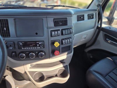 Peterbilt 579 dashboard area showing center console with switches, climate controls, and a yellow hazard sticker; passenger-side dashboard visible.