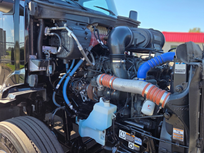 Peterbilt 579 engine bay showing blue coolant reservoir, blue hoses, turbo, intake tubing, and various engine components.