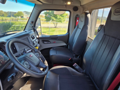 Peterbilt 579 truck cab interior showing driver's seat and passenger seat with black leather, dashboard, steering wheel, and window.