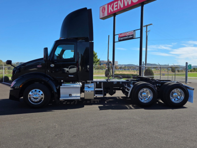 Peterbilt 579 conventional daycab truck in profile view with hood open; chrome wheels; fuel tanks; no cargo; no trailer attached. Visible text includes Kenworth sign in background.