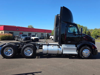 Peterbilt 579 conventional daycab tractor side view showing fuel tanks and chrome wheels, black cab, hood raised by aerodynamic air intake, three rear axles, blue sky.