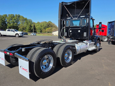 Peterbilt 579 truck chassis in a lot showing dual rear axles and bed area; cab with raised sleeper, black outer surfaces, chrome wheels, and fuel tanks visible.