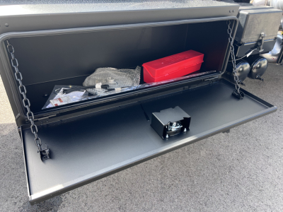 Mack GR64B roll-off truck storage compartment open showing toolbox and red toolbox bin inside.