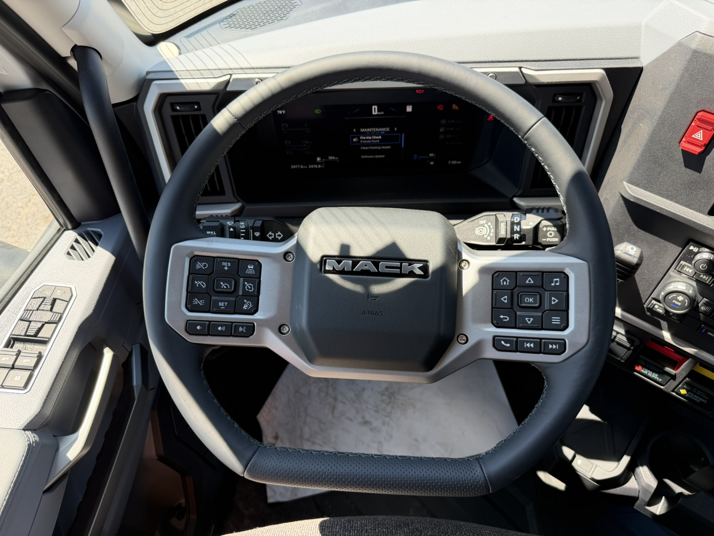 Mack PR64T76H truck interior showing steering wheel with Mack logo and digital instrument cluster.