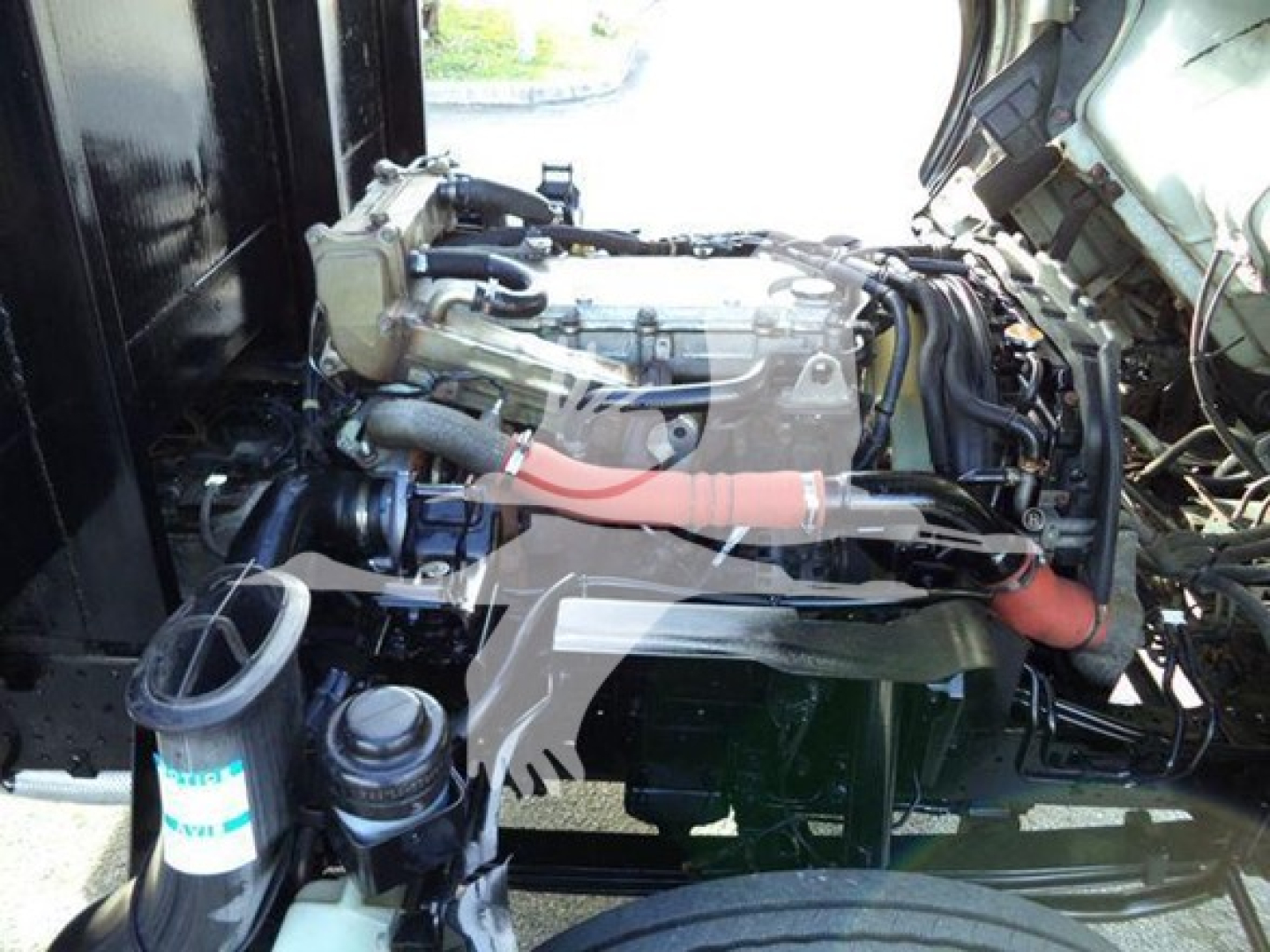 Isuzu NRR engine bay showing Diesel engine with red insulated hose and surrounding components.