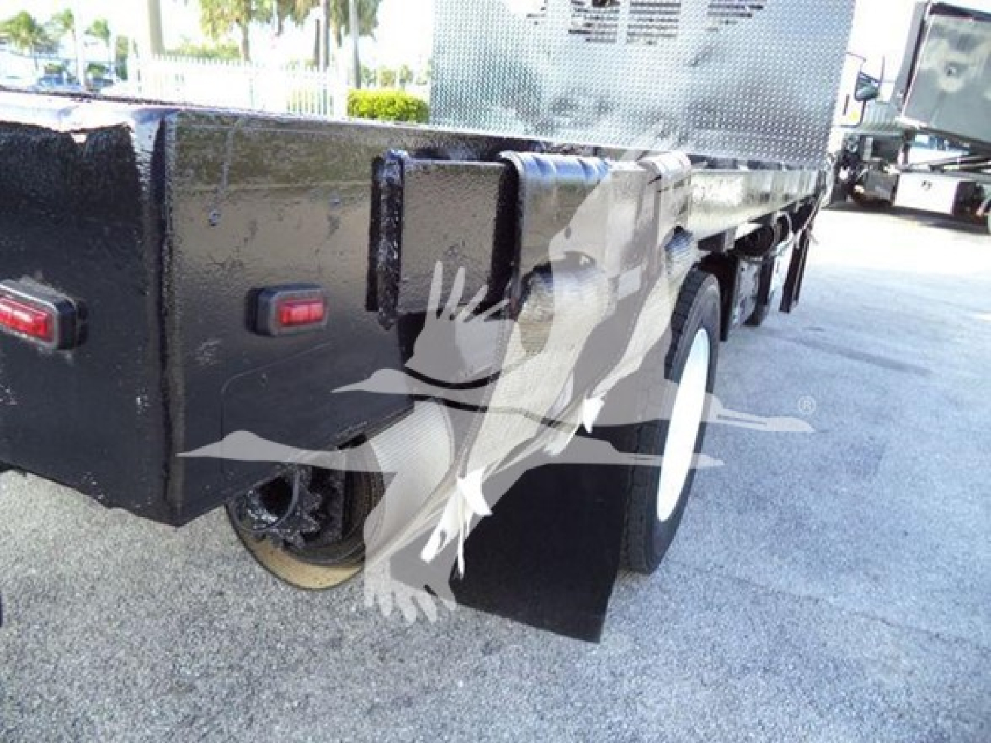 Isuzu NRR flatbed truck rear view showing black chassis, wheel, and mudflap with white graphic overlay.
