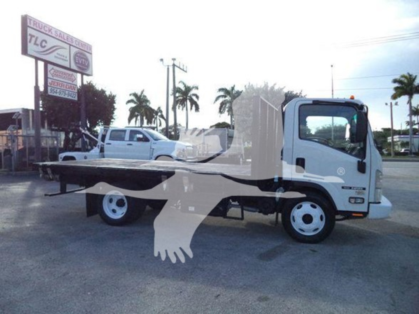 Isuzu NRR flatbed truck side view showing flatbed with white cab, black trim, and surrounding lot.