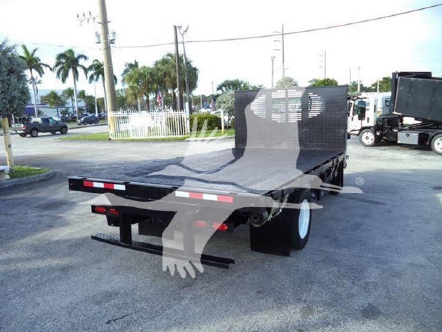 Isuzu NRR flatbed truck rear view showing flatbed and rear bumper, street scene in background.
