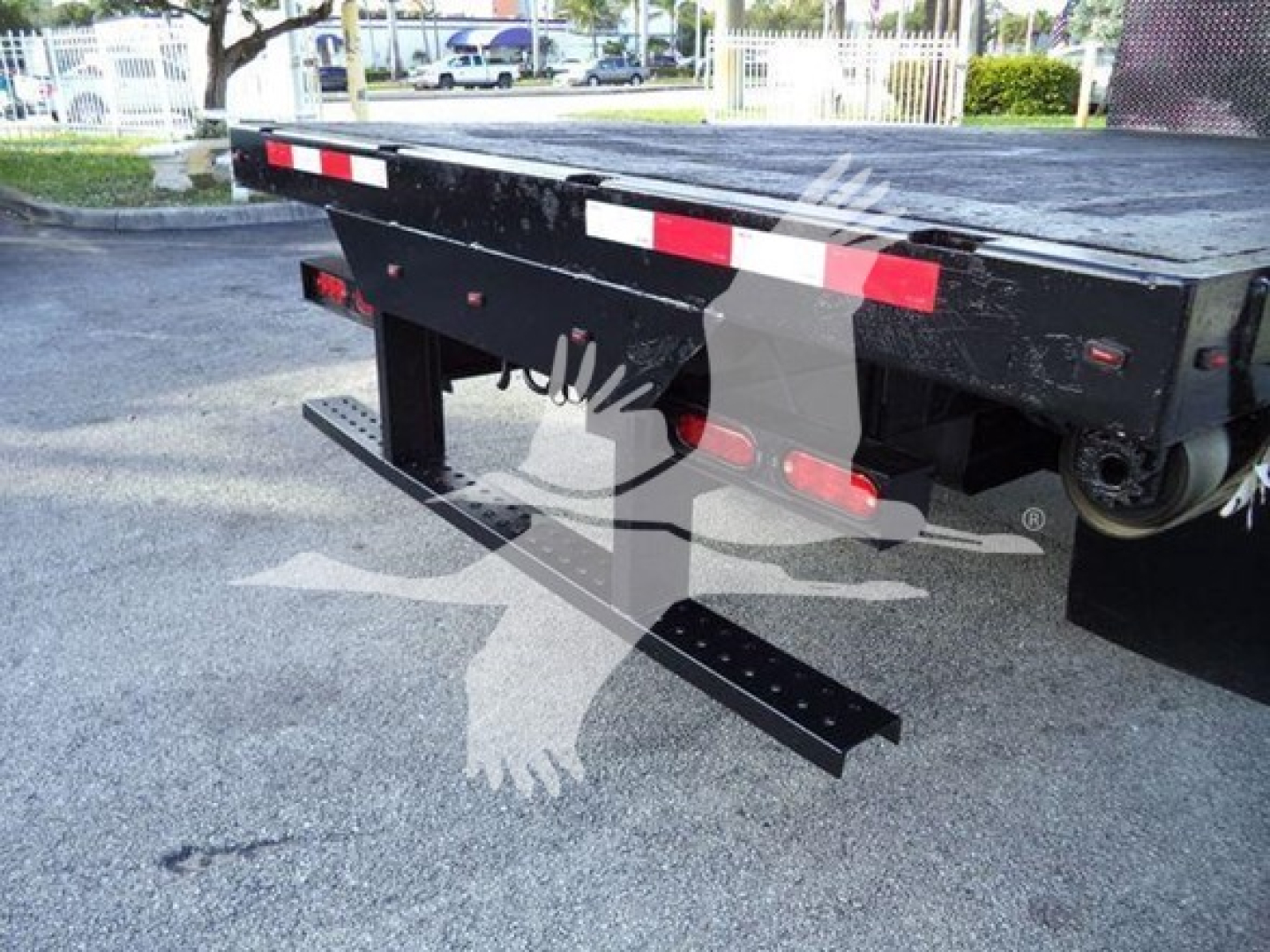 Isuzu flatbed truck rear showing bumper and reflective red/white strips, with black steel underride guard and side rails.