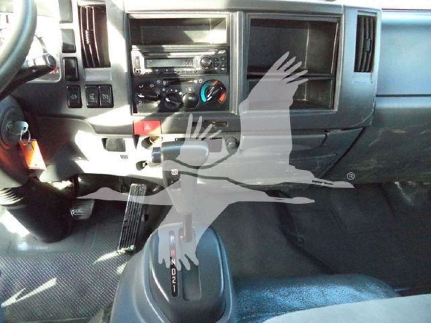 Isuzu NRR truck interior showing center console with climate controls, radio, and gear selector. Partial dashboard and pedals visible.