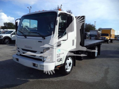 Isuzu NRR flatbed truck in a lot showing cab and flatbed bed with equipment in background.