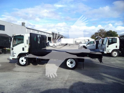 Isuzu flatbed truck in a parking lot with a long black flatbed and white cab; other trucks in background.