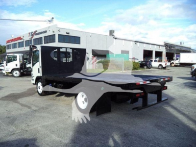 Isuzu NRR flatbed truck in used condition with a drop bed and hydraulic tilt mechanism, side cab visible, dealership in background.