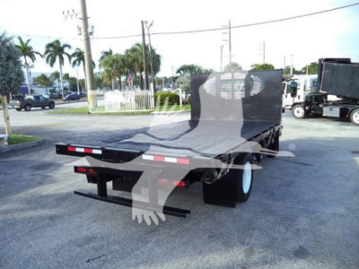 Isuzu NRR flatbed truck rear view showing flatbed and rear bumper, street scene in background.