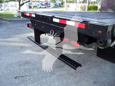 Isuzu flatbed truck rear showing bumper and reflective red/white strips, with black steel underride guard and side rails.
