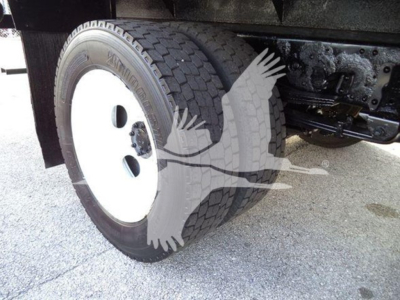 Isuzu NRR truck wheel and suspension visible under flatbed chassis showing white steel wheel, tire, and undercarriage components.