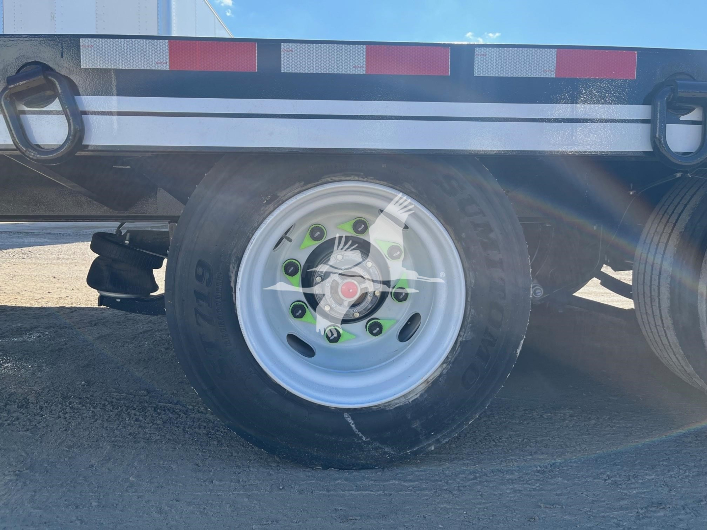 Trailer wheel and undercarriage of a 2025 Eager Beaver 25XPL trailer showing a white steel wheel with green lug nut covers and a black tire. Visible text includes SL087993 on the stock number area and reflective tape on the side rail.