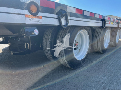 Trailer axle area showing dual wheels and rear frame; visible text includes warning label and circular gauge on the side of the trailer.
