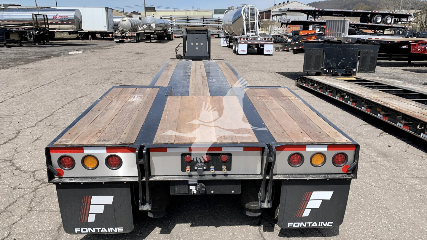 Fontaine Renegade lowboy trailer rear view showing taillights, mud flaps with Fontaine logo, and rear deck with wooden planks and metal beams.