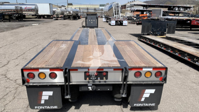 Fontaine Renegade lowboy trailer rear view showing taillights, mud flaps with Fontaine logo, and rear deck with wooden planks and metal beams.