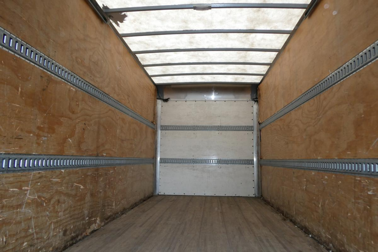 Truck cargo box interior showing wooden walls and metal rails along sides and a closed rear door.