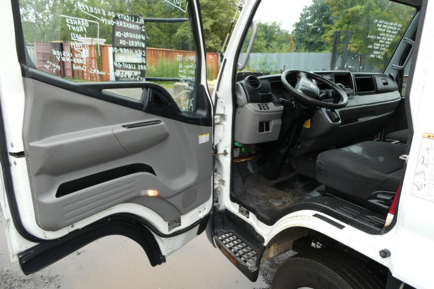 Cab interior of a 2019 Mitsubishi Fuso Canter FE140 truck showing driver seat, steering wheel, and open doors.