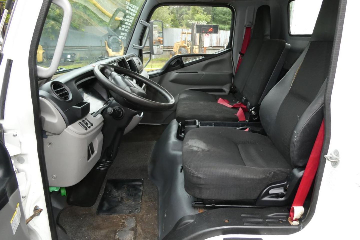 Cab interior of Mitsubishi Fuso Canter FE140 showing driver seat and passenger bench with red seat belts and steering wheel