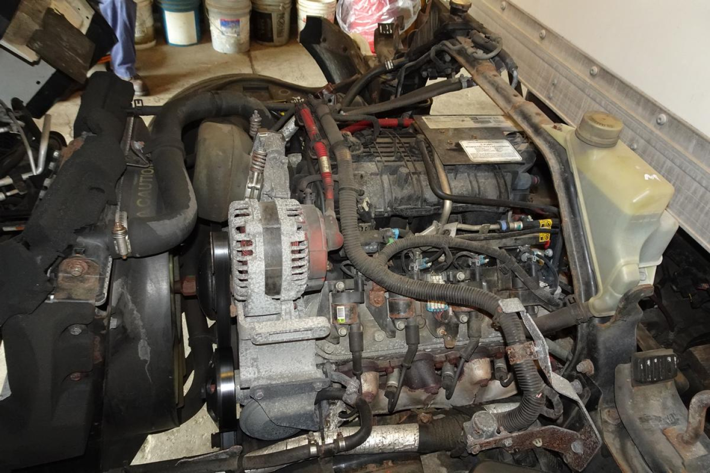 Engine bay of a 2019 Mitsubishi Fuso Canter FE140 showing engine with alternator and hoses; coolant reservoir visible at upper right; various wires and components in view.