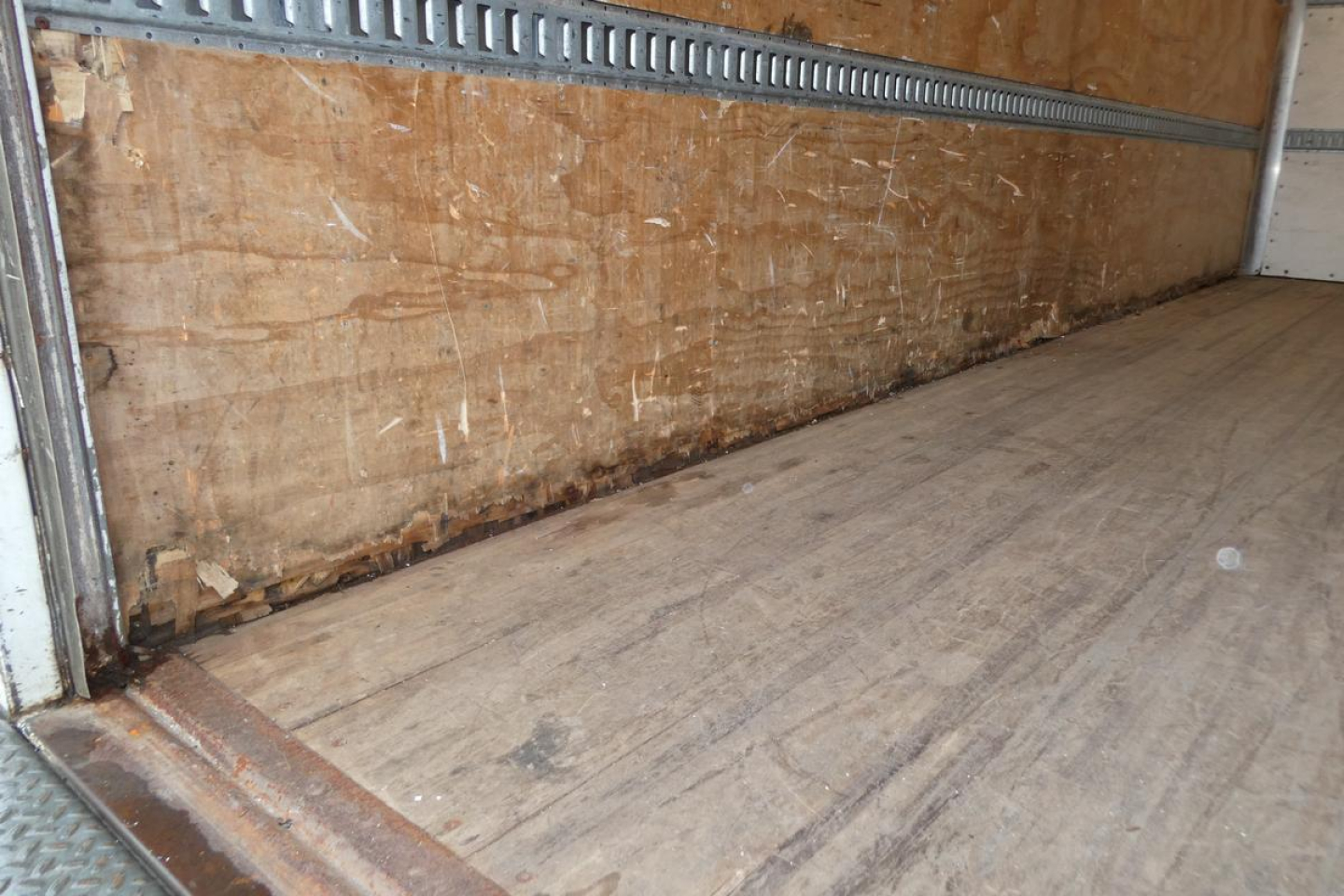 Truck cargo area / box interior showing plywood walls and wooden floor with metal E-track rails along side.