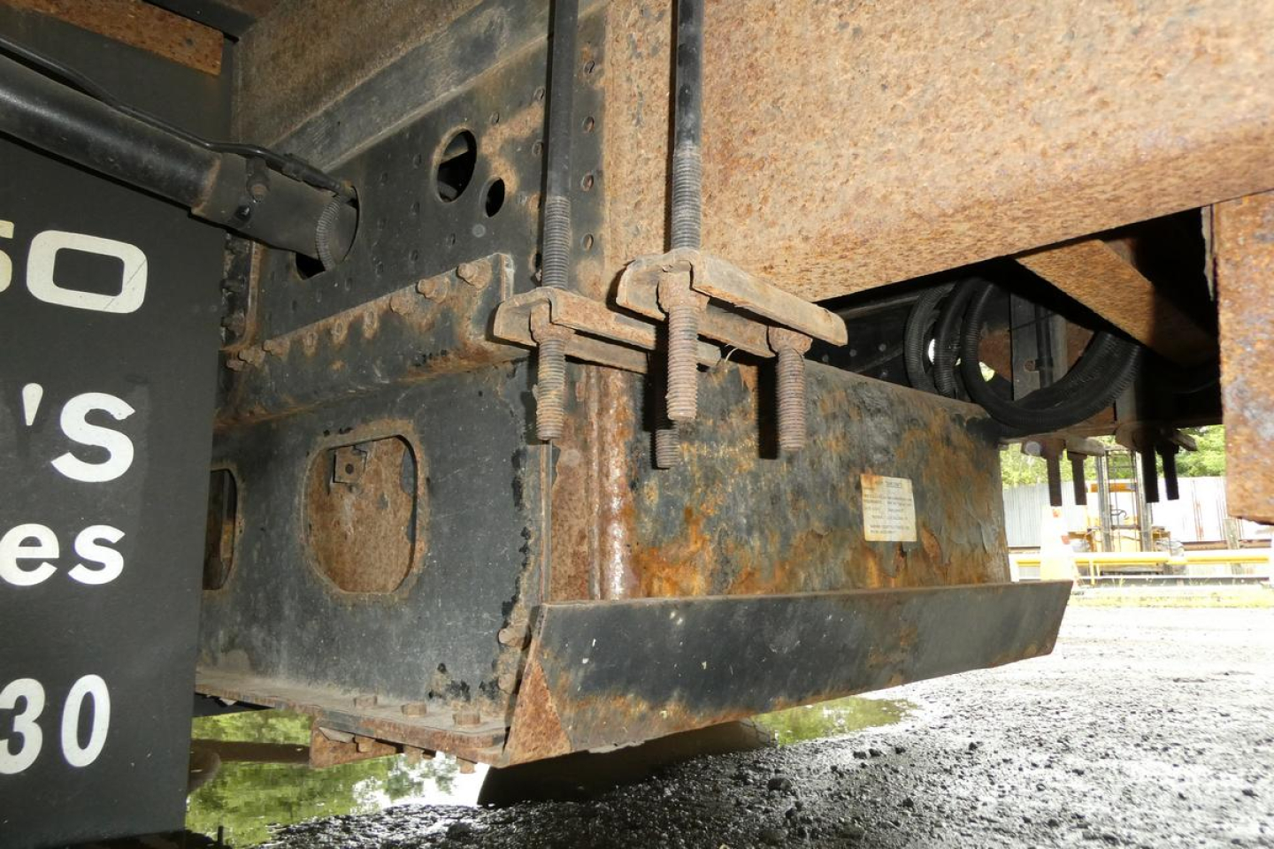 Rear undercarriage of a Mitsubishi Fuso Canter FE140 showing rusted chassis, hitch brackets, and rear bumper with a partial sign visible.