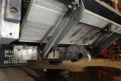 Underside view of a 2019 Mitsubishi Fuso Canter FE140 truck showing undercarriage components and frame with a dented fuel tank and hitch.