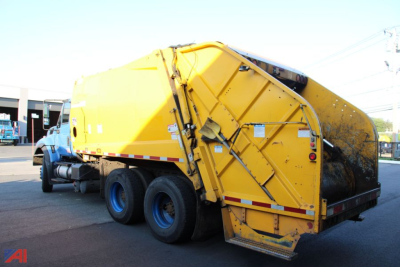 International WorkStar 7400 refuse/roll-off truck with yellow compactor body and blue cab, rear view showing hydraulic arms and warning decals.