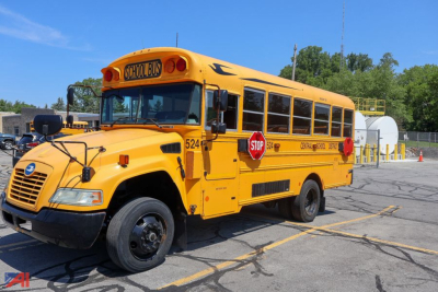 School bus side view showing yellow 2017 Blue Bird Vision mid-size bus with stop sign extended and door closed.