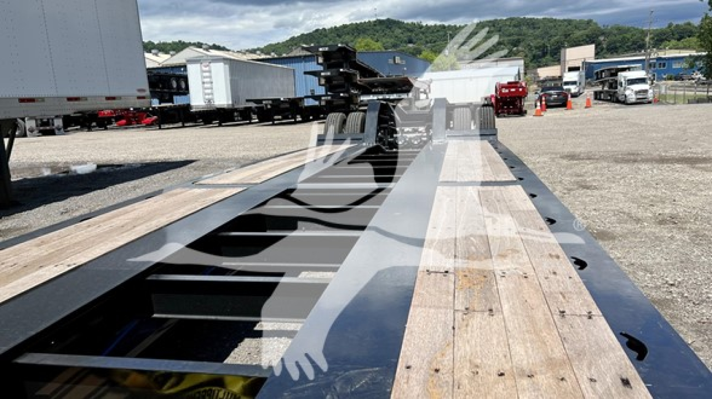 Trailer bed of a lowboy trailer with wooden deck and metal frame, long perspective showing tie-down anchors and cutouts for wheels, XL Specialized XL110HDGS appears in listing.
