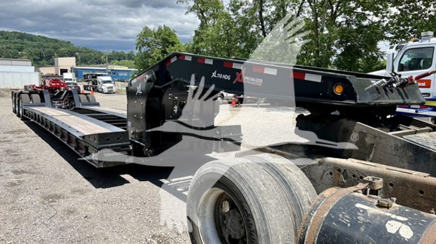 Trailer underside and deck of a lowboy trailer showing structural beams and wheel hub. Visible text includes XL Specialized XL110HDGS on the side.