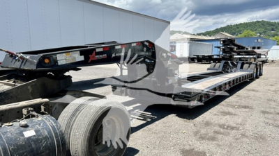 Lowboy trailer in yard with twin axles, brand label visible ‘XL Specialized’ and trailer components; includes steel frame, wheels, and gooseneck area.