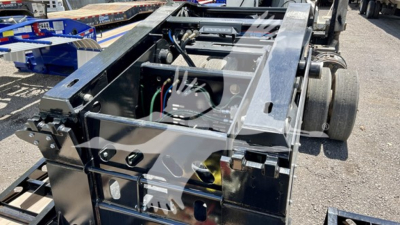 Trailer chassis showing hydraulic components and wiring harness with metal frame and footholds; multiple cables visible; part of a lowboy trailer structure.
