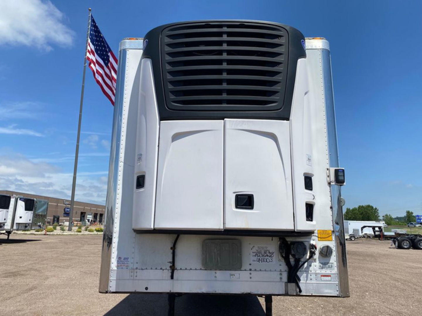 Refrigerated trailer rear view showing Thermo King unit on a 2021 Utility Reefer with flag in background and stock number U91003.