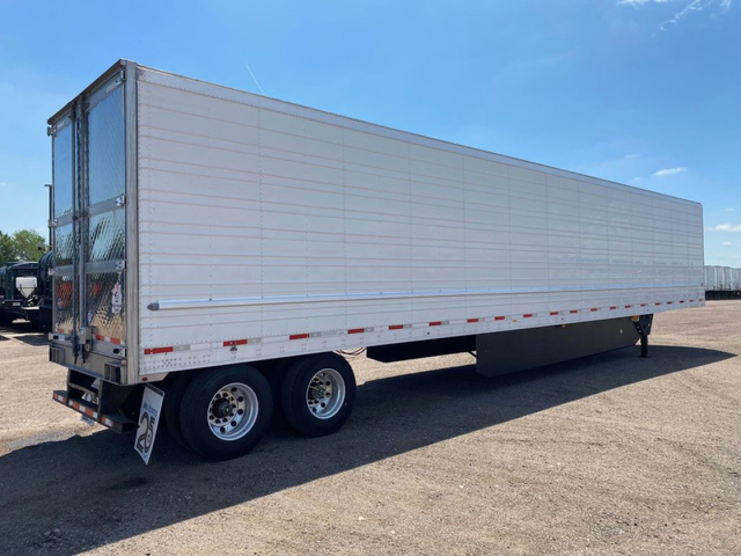 Utility reefer trailer showing white aluminum side panels and tandem rear axles with dual wheels.
