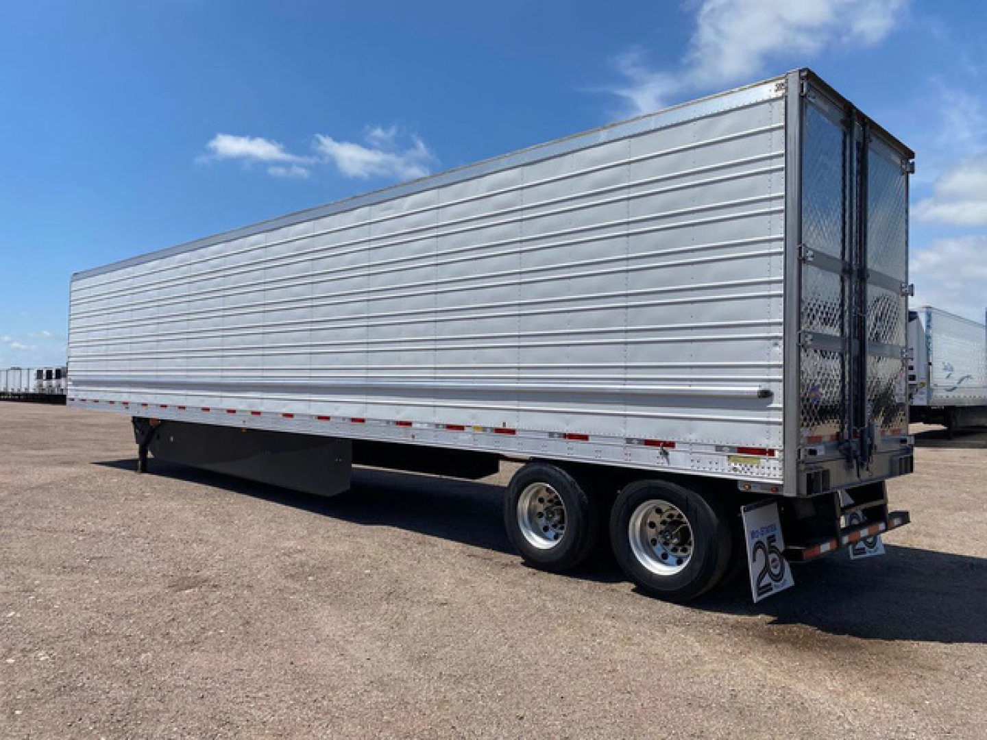 Semi-trailer in utility reefer configuration showing aluminum side panels and dual rear axles with a hinged rear gate.