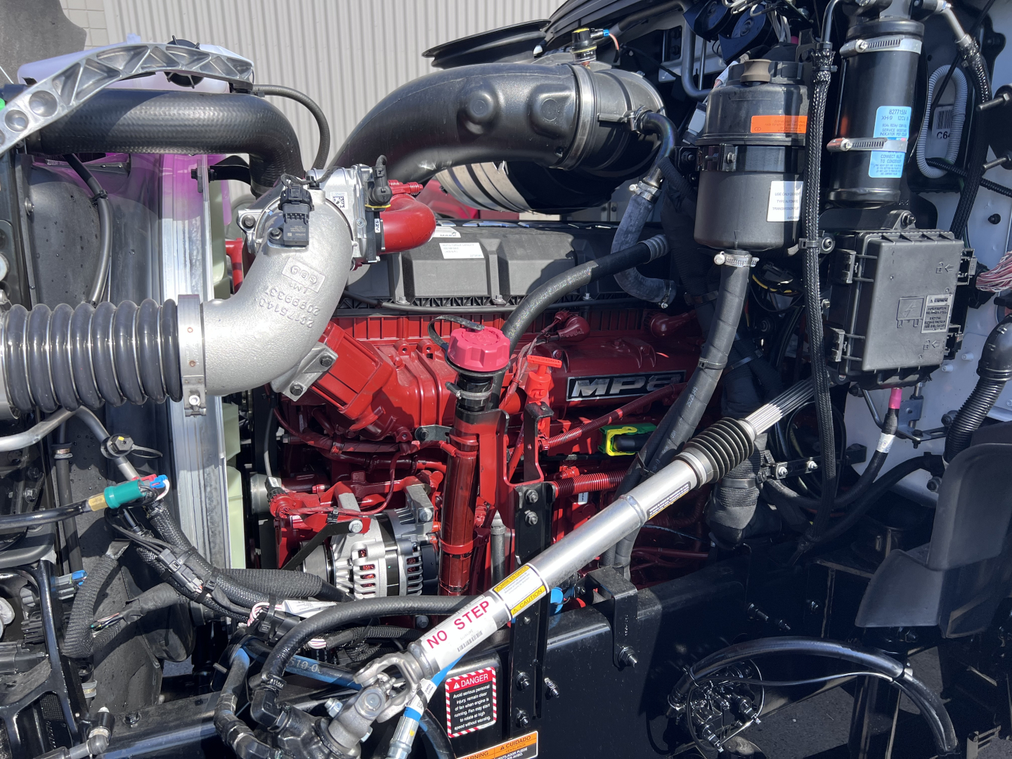 Mack GR64B engine bay showing red engine block, radiator hose, various hoses, and auxiliary components.