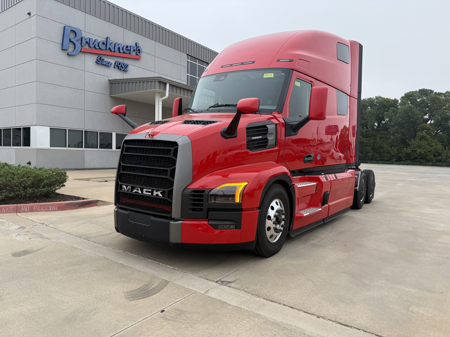 Truck front/side view of a red 2026 Mack PR64T76H conventional sleeper in a dealership lot.