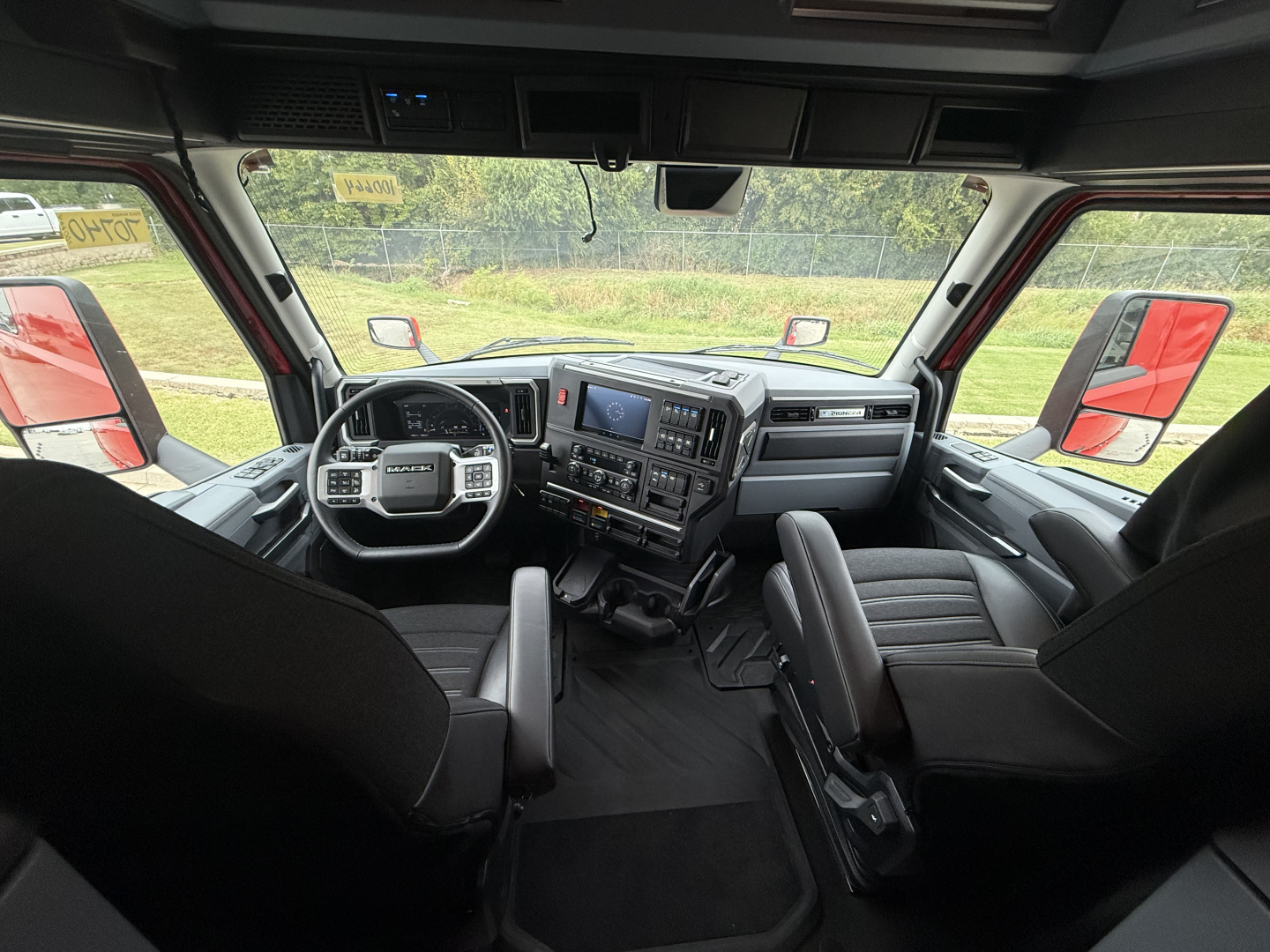 Cab interior of a 2026 Mack PR64T76H truck showing steering wheel, dash, center console, and two captain chairs.