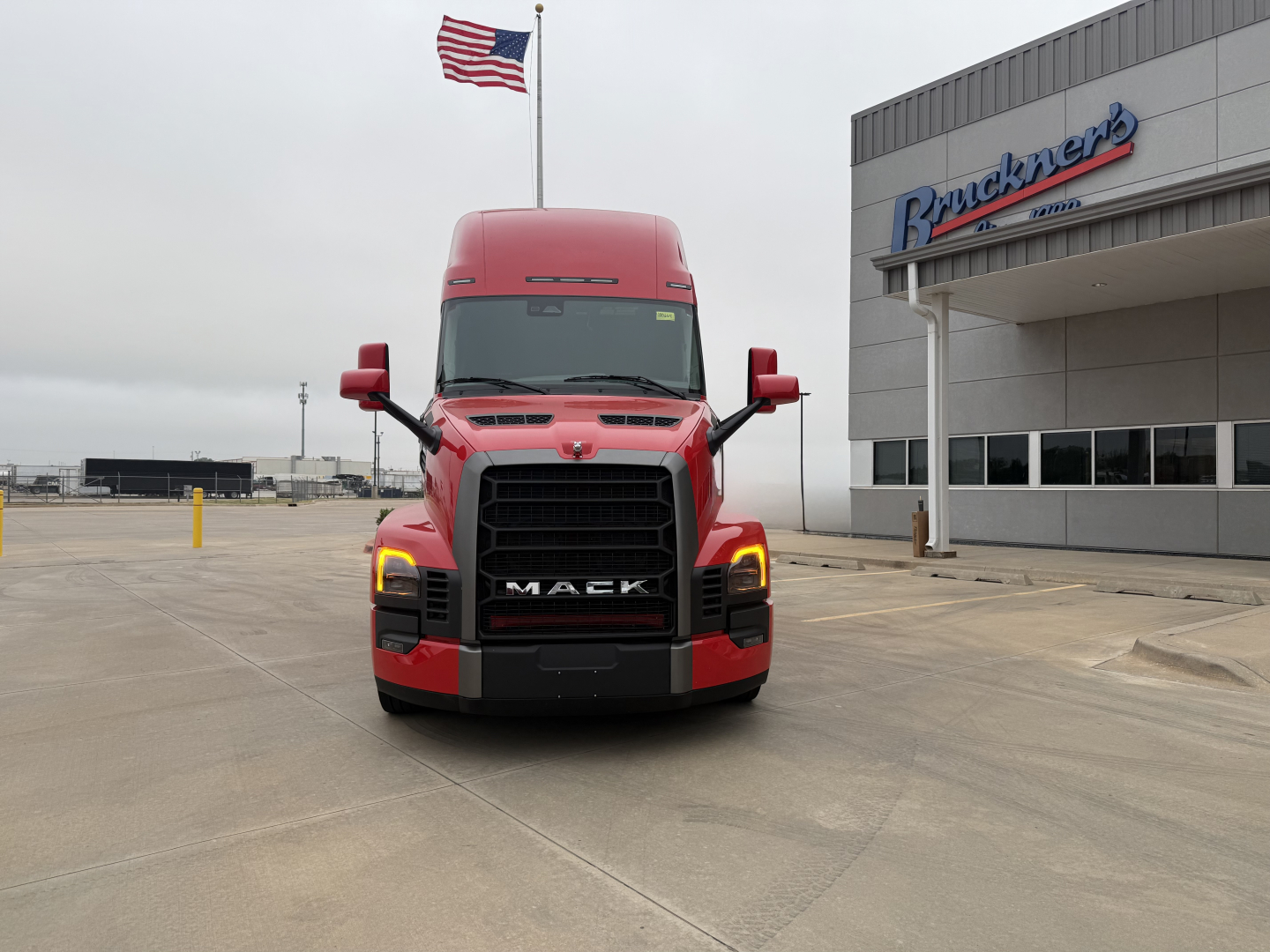 Mack PR64T76H conventional sleeper truck front view with red cab and Bruchner's dealership building in background.