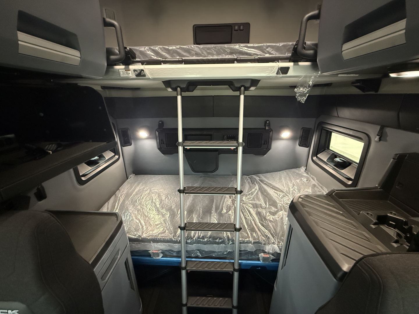 Truck cab interior showing bunk bed with ladder, overhead storage, and windows in a Mack PR64T76H sleeper tractor.